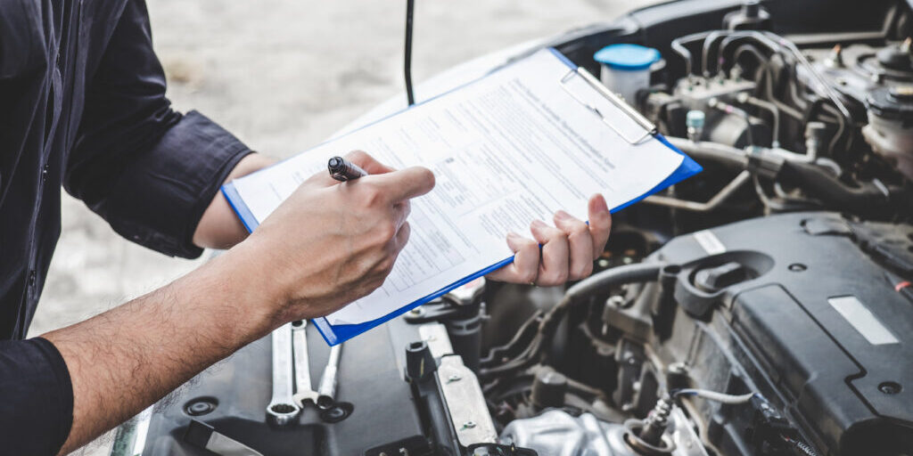 Services car engine machine concept, Automobile mechanic repairman checking a car engine with inspecting writing to the clipboard the checklist for repair machine, car service and maintenance.