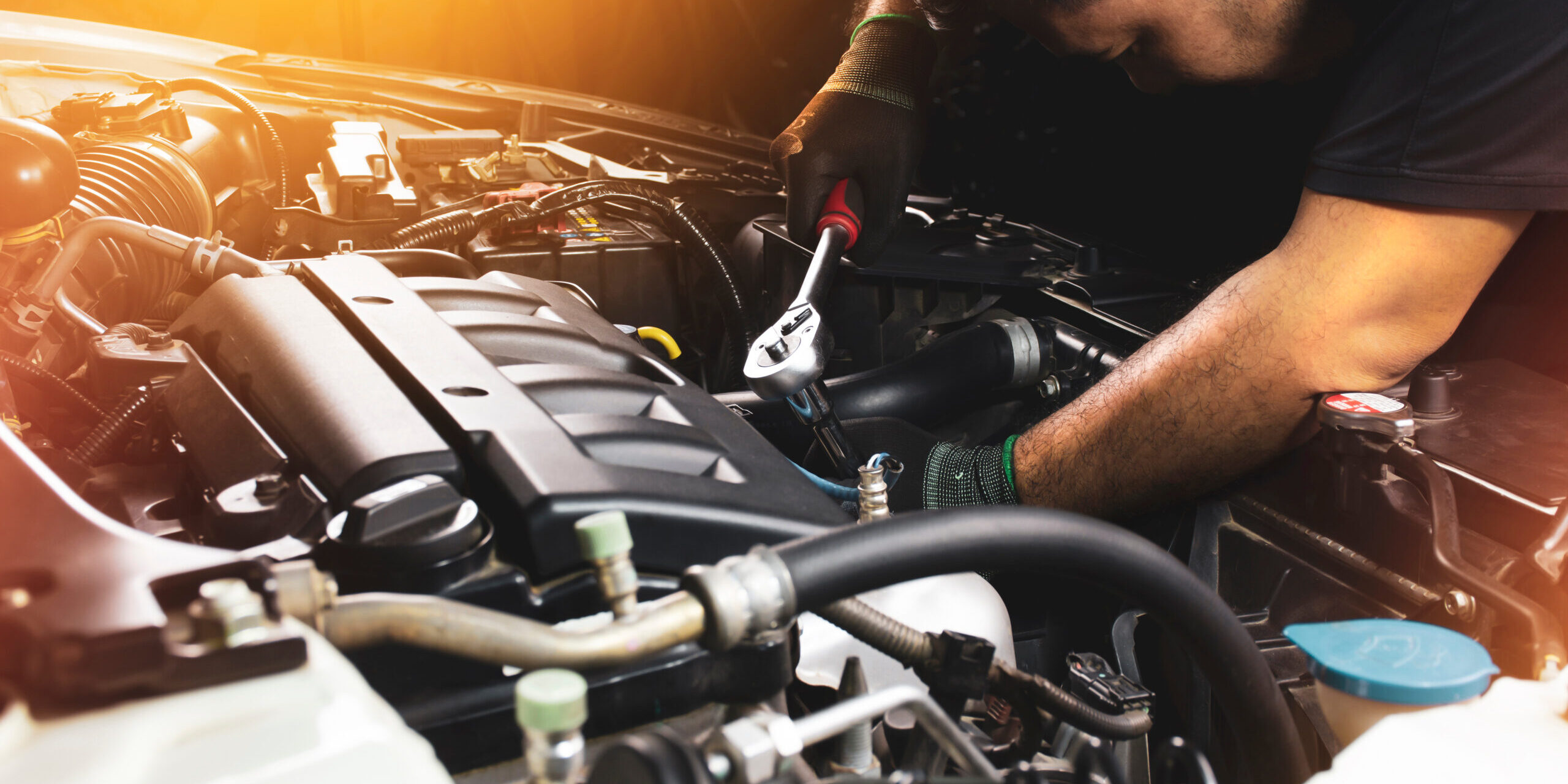 The Mechanic hand wearing black gloves is fasten the bolt with the socket wrench to repairing of the car engine